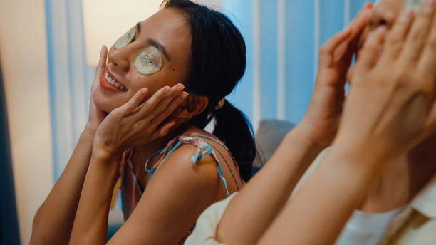 Close-up Young Asia female lesbian in living room. Happy girls relaxing use cucumber eyes mask patch together lay on cozy sofa couch at night. Close-up Young Asia female lesbian in living room. Happy girls relaxing use cucumber eyes mask patch together lay on cozy sofa couch at night. Couple lifestyle at home, friendship and leisure concept. women facial mask mud cucumber stock pictures, royalty-free photos & images