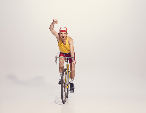 Portrait of young man in colorful clothes, uniform riding bike isolated on grey background. Sportsman. Winning racer. Concept of sport, hobby, work, active lifestyle, retro fashion. Copy space for ad