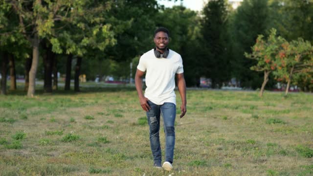 African American man walks in green city park on lawn
