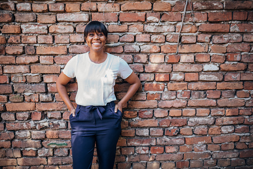 One woman, portrait of a charming black woman standing in front of a brick wall outdoors.