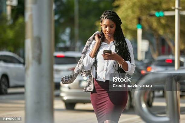 Businesswoman Checking Smart Phone While Walking Downtown Stock Photo - Download Image Now