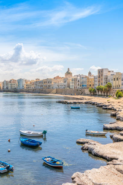 View of old town Trapani coastline: simple fishermen houses facing the sea, with little rowing blue boats awaiting anchored into the shallow water of the bay.