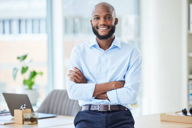 hombre de negocios confiado de pie con los brazos cruzados en una oficina, luciendo orgulloso y feliz solo en el trabajo. retrato de un jefe africano sonriente, alegre y profesional que trabaja en empresas - businessman fotografías e imágenes de stock