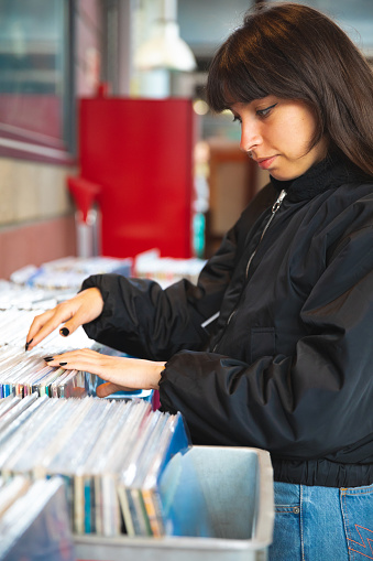 Young woman search vinyl record at flea market stall\n\n+++Note: the location is a free of ticket flea market in Paris (Marche aux Puces, Saint Ouen), is a public space ty+++