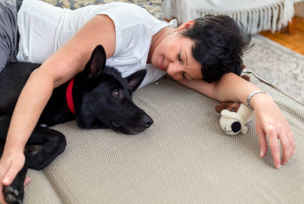 Shoot of a woman lying in bed and cuddling with her dog. She is in bedroom and wearing pajamas.