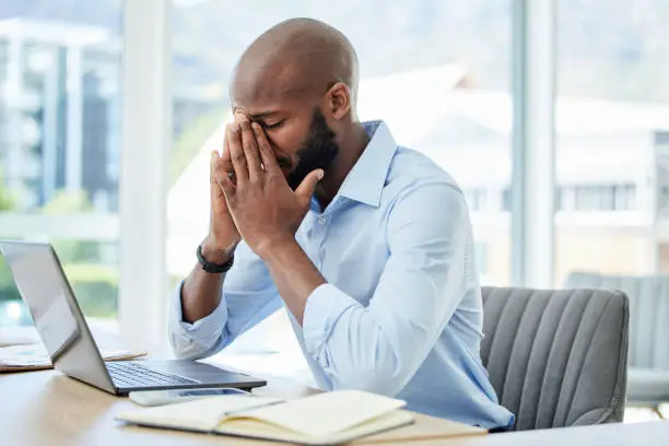 Stress, anxiety and worry with a business man suffering from a headache, migraine or mental fatigue and burnout. Young male working in his office, feeling the pressure of a deadline and struggling