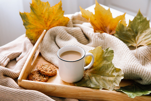 Autumn home still life: a cup of coffee, a warm sweater and yellow leaves. Seasonal breakfast, morning coffee. The concept of home comfort and cozy atmosphere.