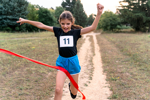 Cute girl runner crossing finish line in a race competition in nature.