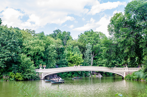 Bow Bridge in Central Park during summer day with people in rowboat on the lake