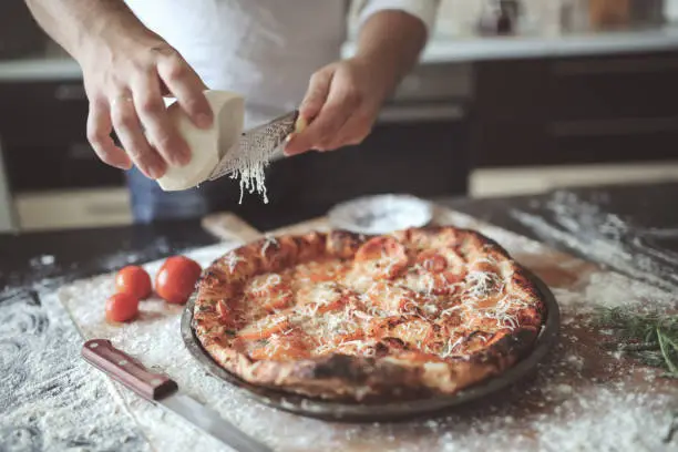 Photo of male hands rubbed cheese grated on pizza in home