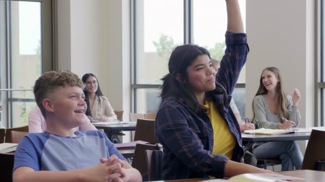 Teen girl at front of classroom raises hand