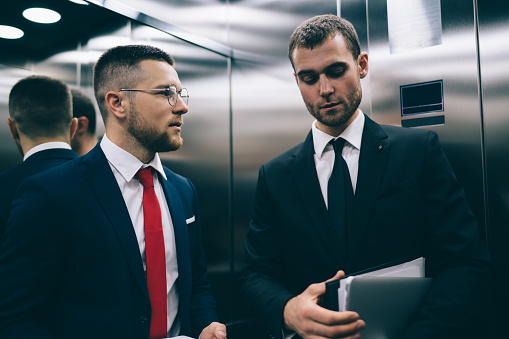 Professional business colleagues having a conversation while commuting on a modern escalator in the urban city environment in their white collar office attire