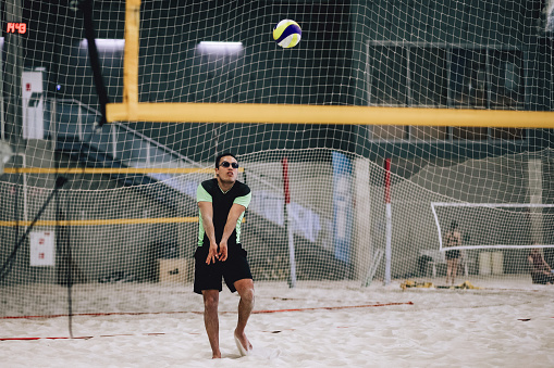 Male portrait of man who playing beach volleyball indoors. Lifestyle sports photography with people. Multiracial person wear sunglasses with ball in gym like sport court