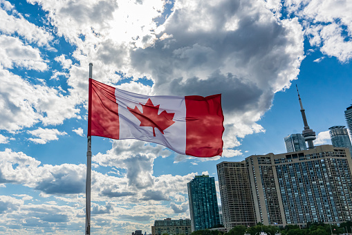 Canada Day flag with maple leaf on background of Montreal city. Red canadian symbol over buildings of Montreal town at Canada National Day of 1st July. Happy Canada Holiday celebrated in summer season.