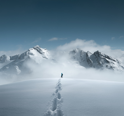Man hiking in fresh snow and enjoying amazing views. Footprints are visible in the snow.