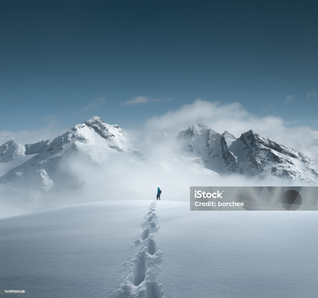 Mountain Hiking Man hiking in fresh snow and enjoying amazing views. Footprints are visible in the snow. Mountain Stock Photo
