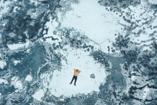Aerial view on a man lying on a cracking ice on a frozen lake.