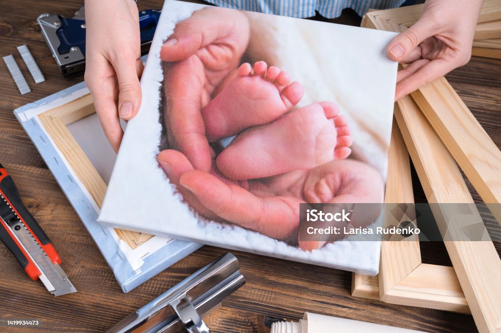 The master demonstrates a photo of children's legs printed on canvas and stretched on a stretcher. Artist's Canvas Stock Photo