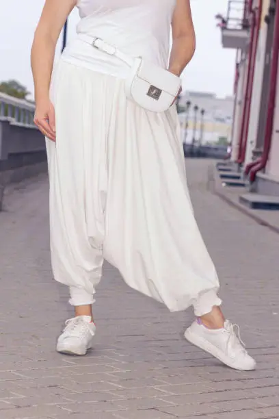 Plus size woman posing against the backdrop of the city in white oriental harem pants.