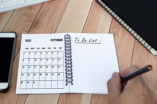 Businessman hands with pen writing to do list with October 2023 calendar on notebook. Copy space. Business concept.