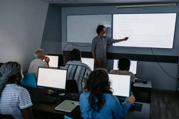 Young Male Teacher Teaching A Programing Class Young male teacher teaching young students a programming class in the classroom. teacher projector stock pictures, royalty-free photos & images