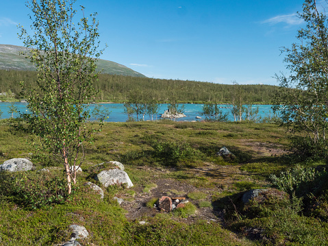 Beatiful camping spot in northern landscape in Swedish Lapland with turquoise blue Vuojatadno river, birch tree forest and green mountains at Padjelantaleden hiking trail. Summer sunny day, blue sky.