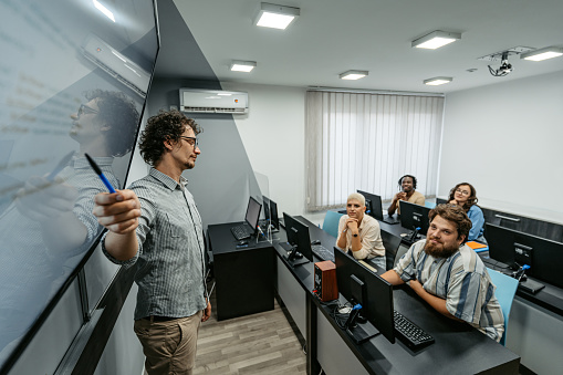 Young male teacher teaching young students a programming class in the classroom.