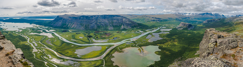 Aerial panoramic scenic view from Skierffe rock summit on glacial Rapadalen river delta valley at Sarek national park with meanders, lakes, mountains, birch trees. Summer day landscape Sweden Lapland.