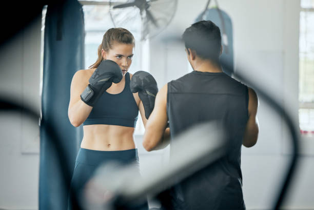ジムでコーチとボクシングフィットネストレーニング、トレーナーと自己防衛を学ぶ怒っている女性、スポーツクラブでウェルネスのための有酸素運動を学ぶ。センターでワークアウトクラ� - men furious boxing combative sport ストックフォトと画像