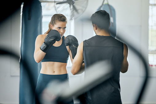 Boxing fitness training with coach at gym, angry woman learning self defense with trainer and learning cardio exercise for wellness at sports club. Male instructor teaching workout class at center
