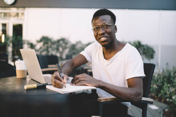 istock Friendly black male writing in notebook and smiling at camera 1419940634