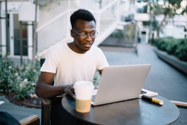 istock Positive dark skinned male freelancer searching information and watching videos from web pages working remotely on cafe terrace, smiling dark skinned man student watching webinar on laptop computer 1419940643