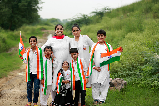 Cheerful Indian family standing together outdoor in nature holding national flag in hands during Independence /Republic day celebration event portrait together outdoor in nature.