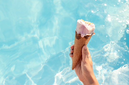 girl hand holding bitten ice cream in waffle cone against water pool