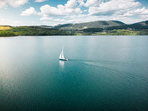 A dreamlike aerial drone shot of a beautiful sailing boat on lake with sparkling waters. The riverscape looks great and gorgeous