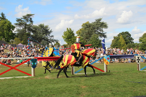 Hever, UK - 29 August, 2022: Re-enactment of a medieval jousting tournament. Knights on horseback ride towards each other carrying lances with the intention of delivering scoring blows or unseating their opponent.