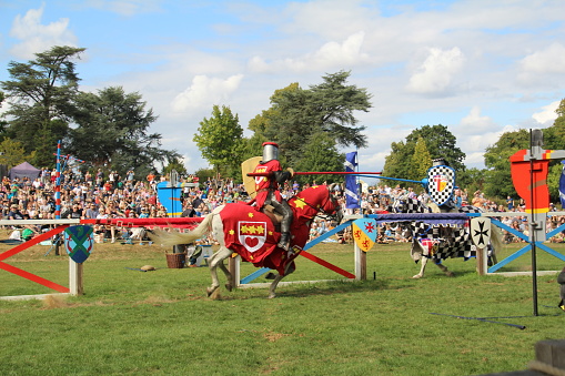 Hever, UK - 29 August, 2022: Re-enactment of a medieval jousting tournament. Knights on horseback ride towards each other carrying lances with the intention of delivering scoring blows or unseating their opponent.