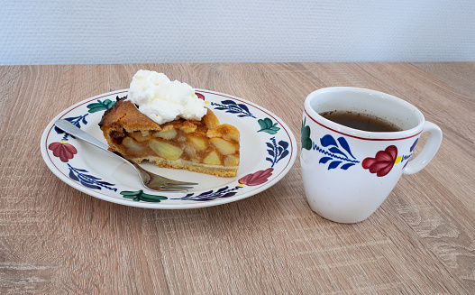 Traditional Dutch apple pie with a cup of coffee. Ceramics are in hand-painted farmer's pattern ('boerenbont') on a wooden table.
