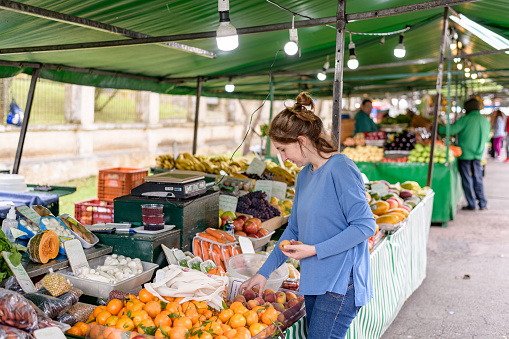 A beautiful young woman choosing peaches at a farmer's food market stall. For a more sustainable world, the purchase is carried in a canvas bag.