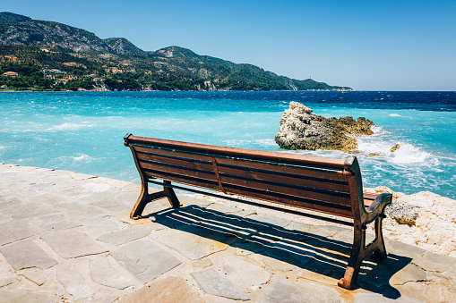Public bench in Kokkari village, Samos island, Dodecanese, Greece in afternoon. Selective focus on rock in the sea.