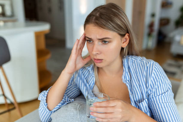 istock Depressed young woman having headache while drinking water on sofa at home. 1419956492