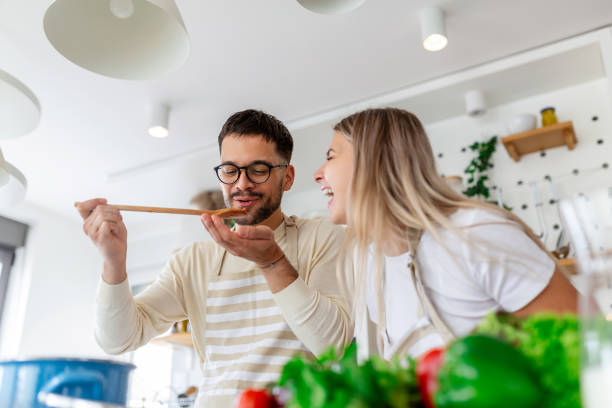 istock Beautiful young couple is looking at each other and feeding each other with smiles while cooking in kitchen at home. Loving joyful young couple embracing and cooking together, having fun in the kitchen 1419956543