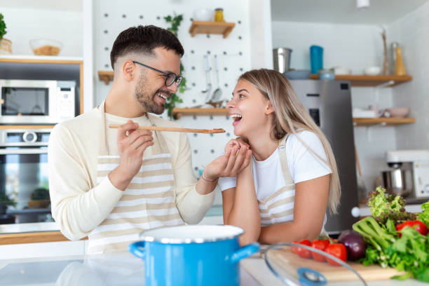 istock Beautiful young couple is looking at each other and feeding each other with smiles while cooking in kitchen at home. Loving joyful young couple embracing and cooking together, having fun in the kitchen 1419956546