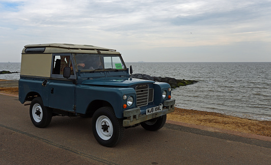 Felixstowe, Suffolk, England - May 01, 2022:  Classic Blue Land Rover being driven along seafront promenade ocean in background.