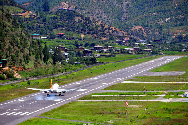 Paro airport - runway, aircraft touchdown, Bhutan Paro, Bhutan: touchdown of an Airbus A319 lands at Paro International Airport - smoke from the tires -  the only international airport in Bhutan, located in a deep valley along the river Paro Chhu, near peaks as high as 5,500m (18,000 ft), it is considered one of the world's most difficult airports, flights operate only in visual meteorological conditions (VMC), an aviation flight category in which visual flight rules (VFR) flight is permitted. The airport has a single 2,265 m (7,431 ft) asphalt runway. Very few pilots are certified to land at Paro International Airport. bhutanese culture photos stock pictures, royalty-free photos & images