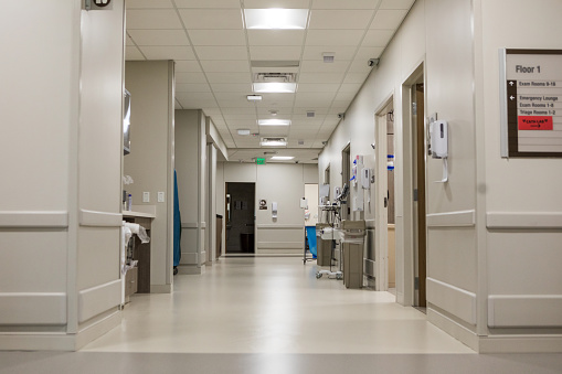 A view down the corridor of the emergency department of the hospital with doorways leading to individual examination rooms and a bathroom at the end of the hall.