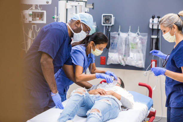 Diverse emergency room team works on female patient The multiracial ER team works on an unrecognizable young adult female patient. triage stock pictures, royalty-free photos & images