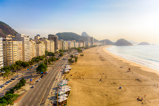 The beach with few people and Avenida Atlântica with the buildings facing the sea at sunrise in a sunny day
