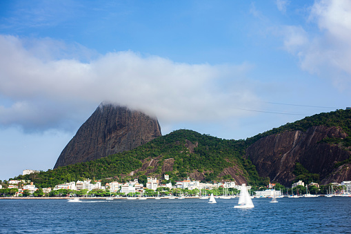 Sugarloaf partially covered by clouds and some boats sailing in front,  in a sunny day