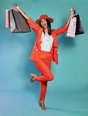 Fun, happy and trendy woman with shopping bags after retail therapy, spending and buying clothes. Stylish, edgy and funky model holding gifts and wearing colorful, fashionable red suit while excited